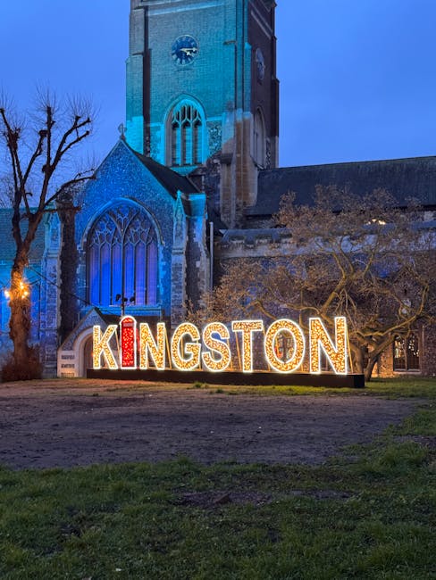 Nighttime view of a historic church with tall stone walls, arched stained glass windows, and a prominent clock tower illuminated by blue lighting. In front of the church, illuminated letters spelling 'KINGSTON' are displayed on the grass, with the letters decorated in red, white, and yellow lights. The scene includes leafless trees and a dark sky, highlighting the vibrant signage and architectural details. Kingston upon Thames Cleaners focuses on surface cleaning, deep cleaning, and sanitisation for residential and commercial spaces, ensuring proper disposal and hygiene as recommended for upholstery and other household items.